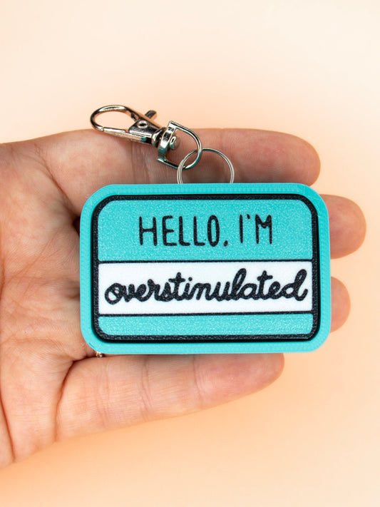 Hello I'm overstimulated keychain top view in hand on orange background