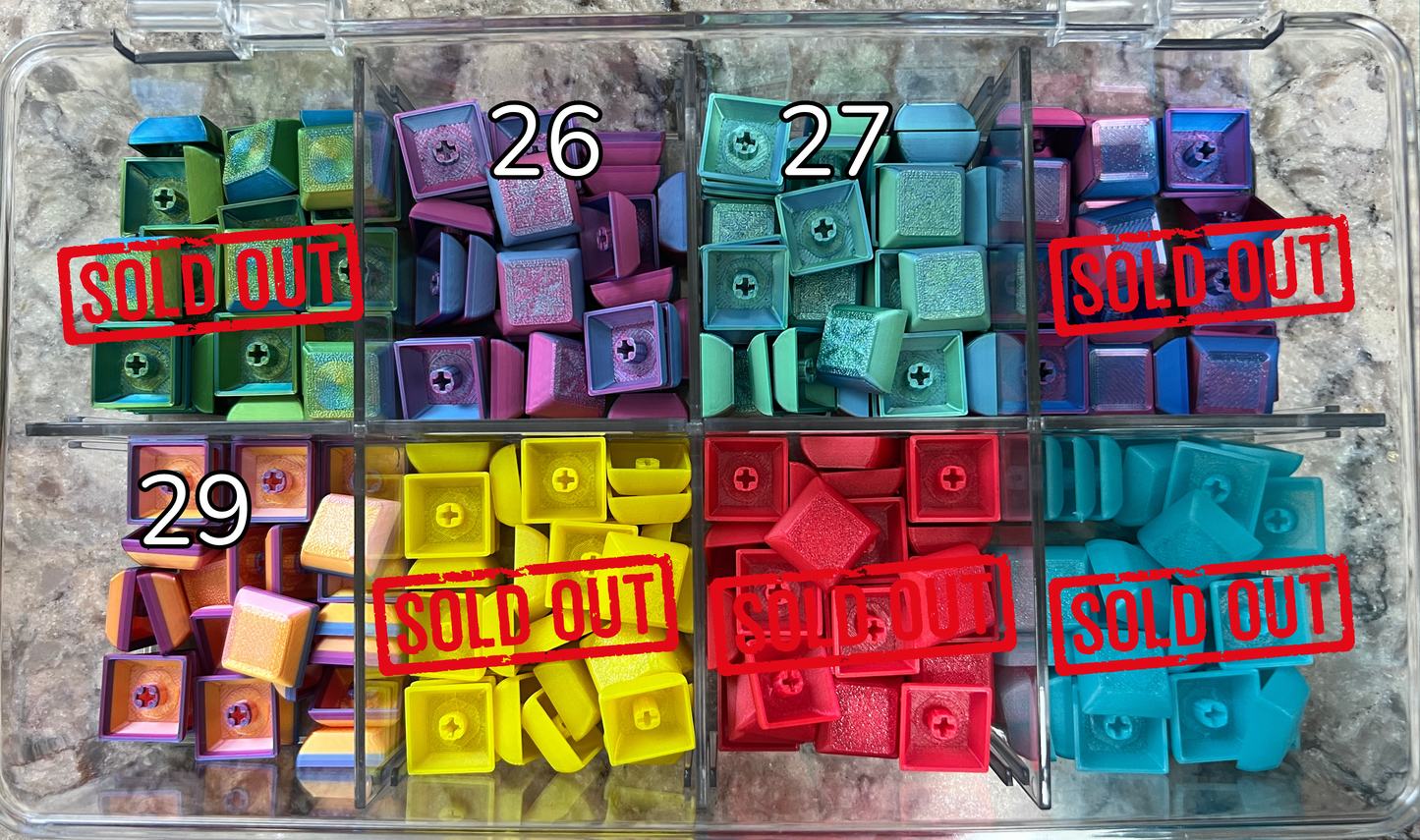 Colorful plastic keyboard caps of various colors numbered. Several options sold out. current options including 26. Purple pink color, 27 aquad marine color 29. Golden orange color with purple blue outline on base. 