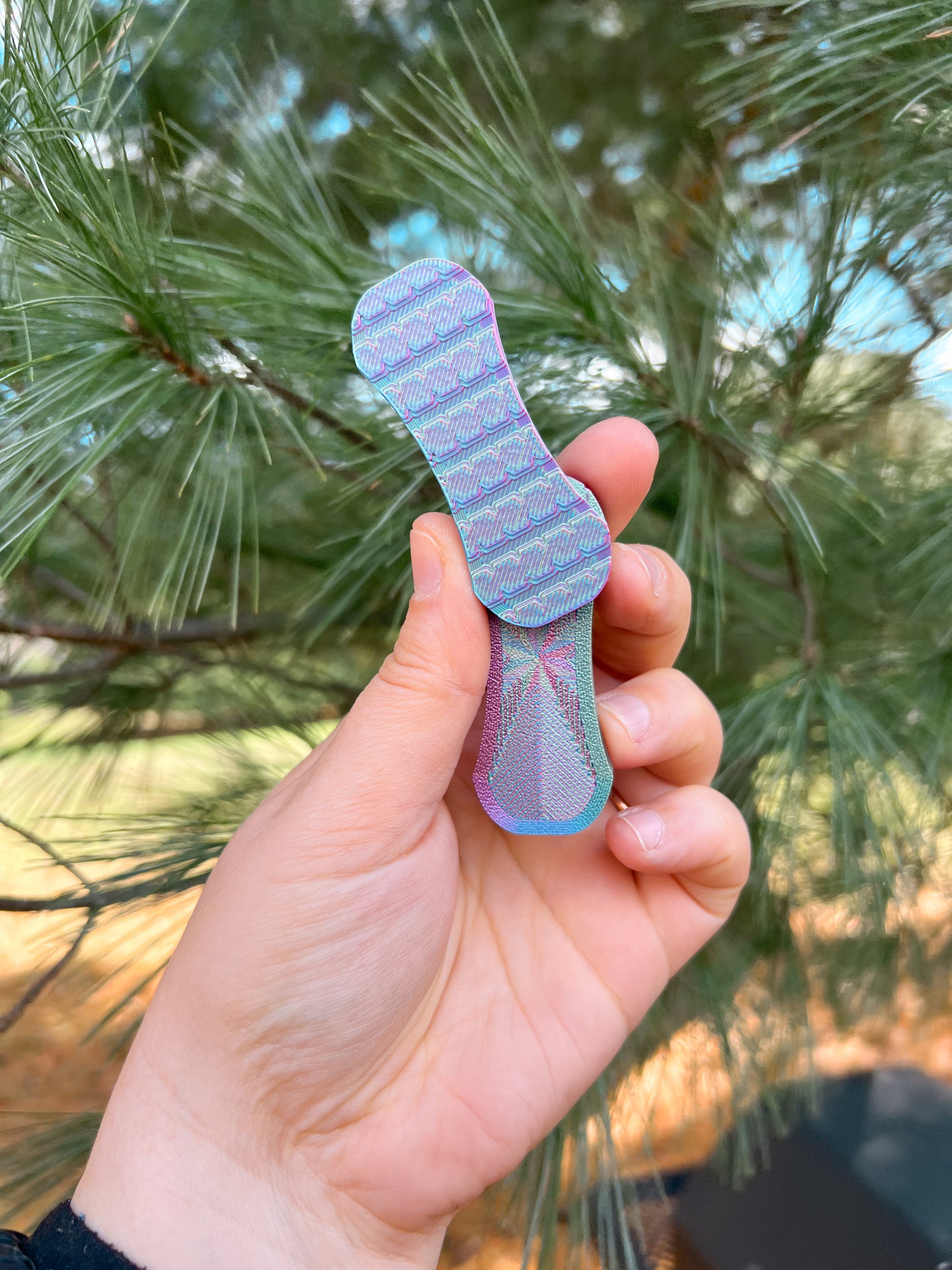 Hand holding a blue and purple magnetic slider fidget against a blurred green outdoor background