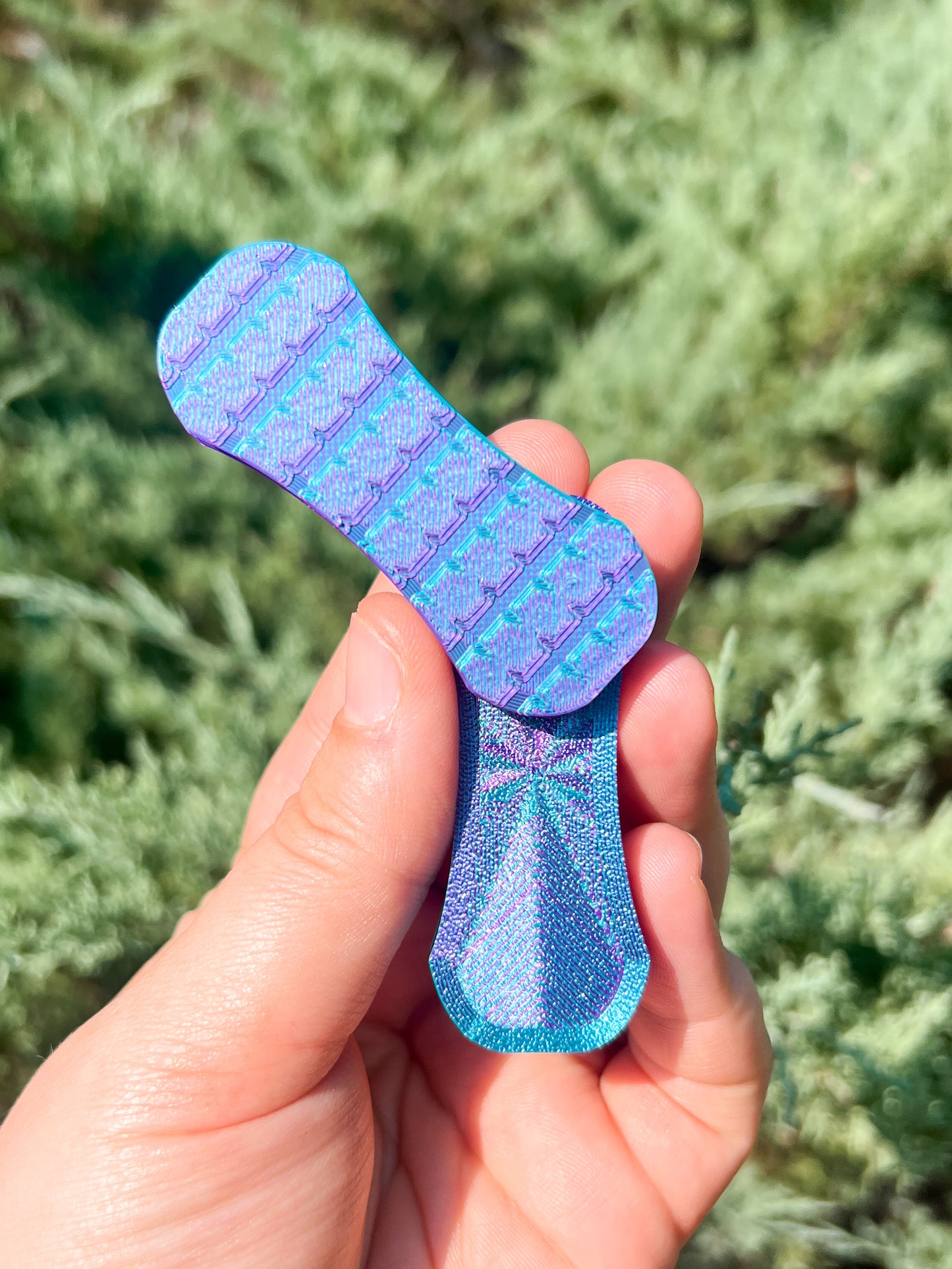 Hand holding a blue and purple patterned object against a green grass background