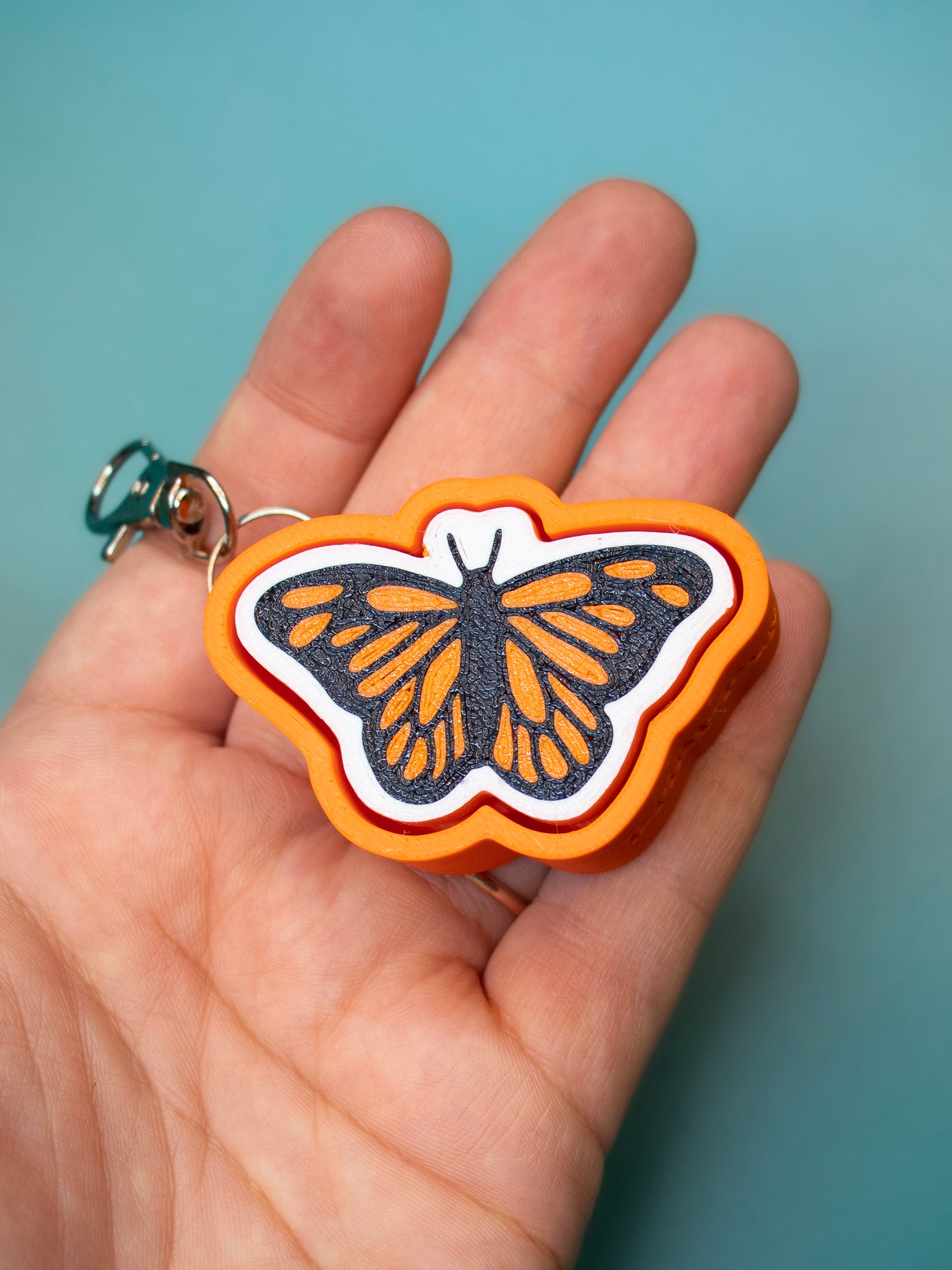 Print Pop Butterfly Keychain in hand with teal background
