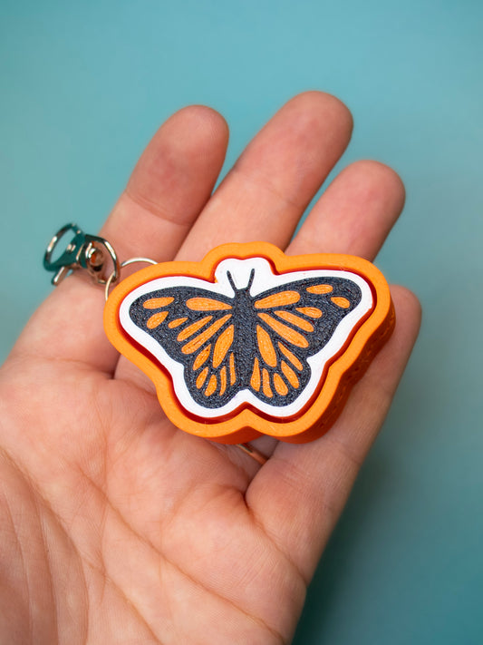 Print Pop Butterfly Keychain in hand with teal background
