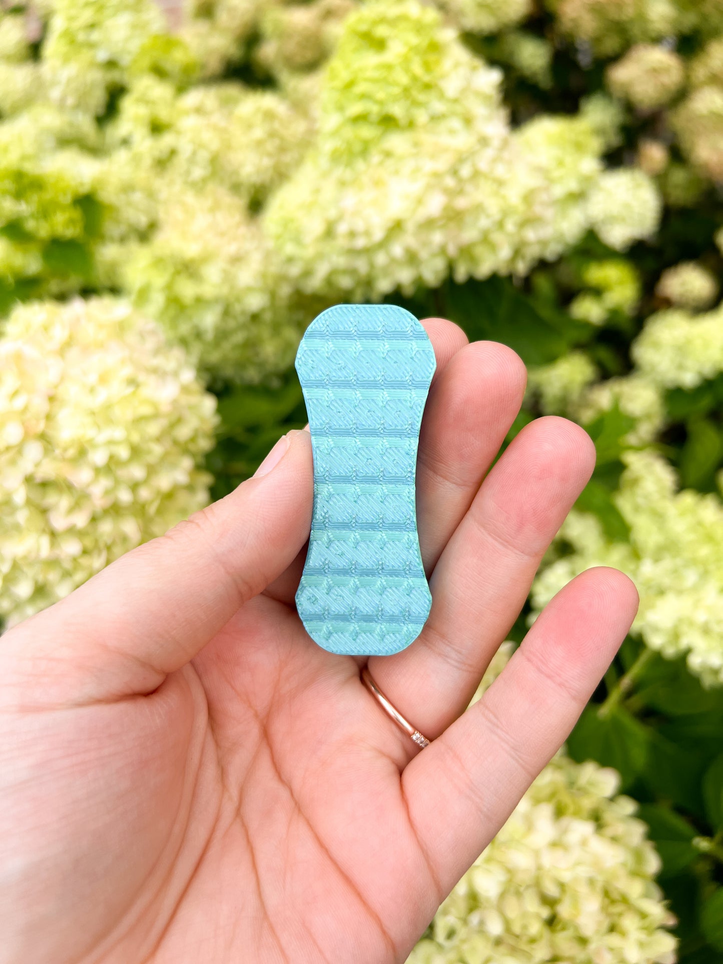 Teal blue mangnetic fidget slider in hand floral background
